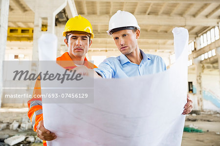 Male architects discussing over blueprint at construction site