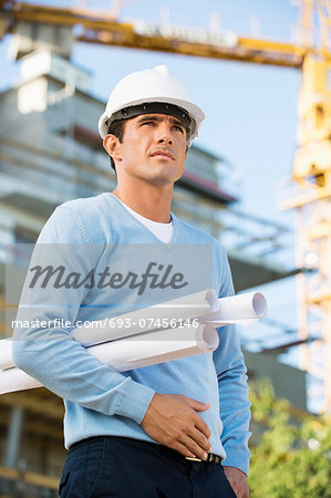 Male architect with rolled up blueprints standing at construction site