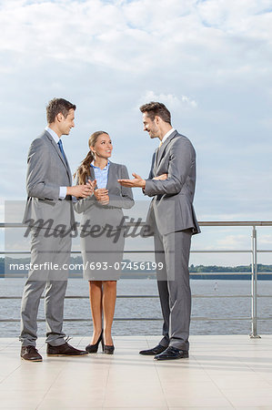 Full length of young businesspeople communicating on terrace against sky
