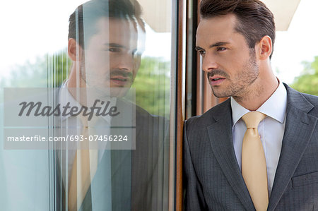 Thoughtful businessman leaning on glass door