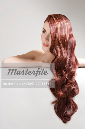 Thoughtful woman with long red dyed hair against gray background