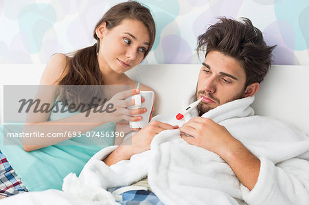 Young woman giving coffee mug to man with thermometer in mouth Young woman giving coffee mug to man with thermometer in mouth
