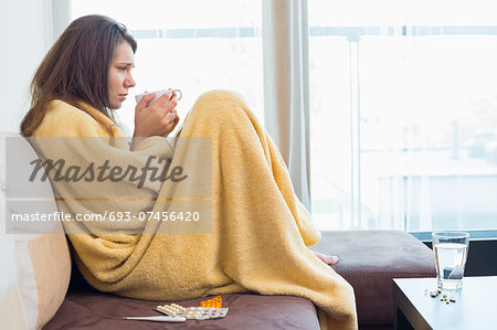 Side view of sick woman having coffee on sofa in living room