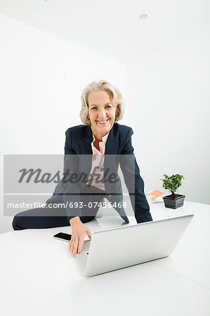 Portrait of senior businesswoman with laptop sitting on desk in office