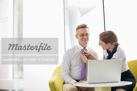 Businesswoman putting on tie to male colleague at lobby