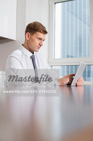 Mid adult businessman using tablet computer at kitchen table
