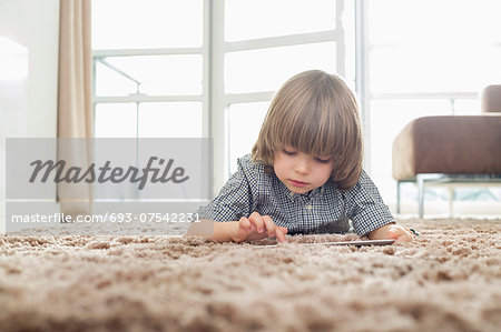 Boy using digital tablet while lying on rug in living room
