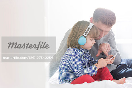 Mid adult father with boy listening music on headphones in bedroom