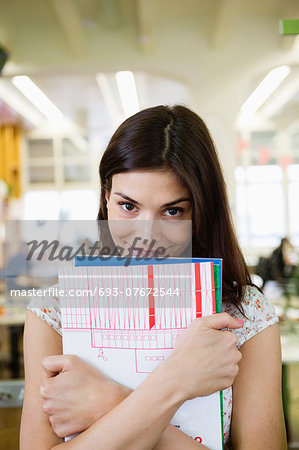 Portrait of happy young businesswoman with books in office