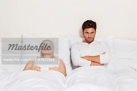 Displeased young man with woman sleeping in bed