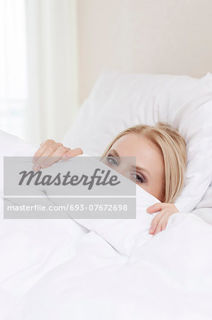 Portrait of shy young woman hiding under bedsheet