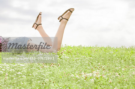Low section of woman lying on grass against sky