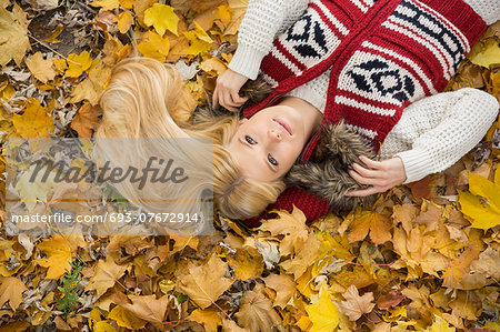 High angle view of thoughtful young woman lying on autumn leaves in park
