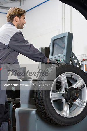 Side view of mid adult male mechanic repairing car's wheel in workshop