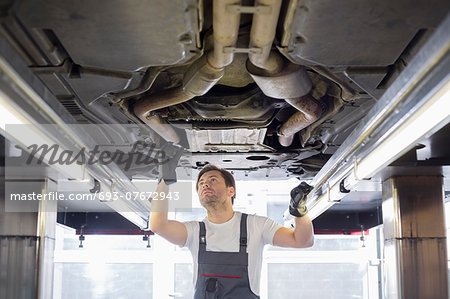 Mid adult male repair worker repairing car in workshop Mid adult male repair worker repairing car in workshop