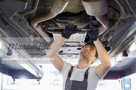 Mid adult automobile mechanic repairing car in workshop Mid adult automobile mechanic repairing car in workshop