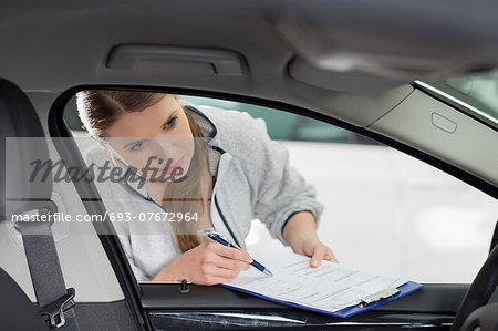 Female maintenance engineer with clipboard examining car's interior in workshop