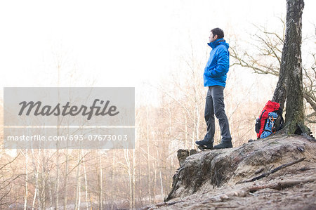 Side view of hiker standing on edge of cliff in forest Side view of hiker standing on edge of cliff in forest