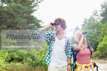 Young couple using binoculars while hiking in forest