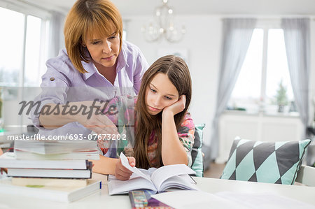 Mother assisting bored girl in studying at home