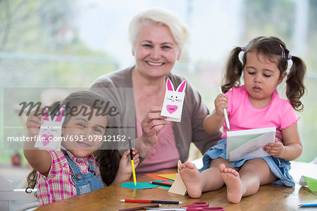 Portrait of happy senior woman showing craft rabbit while sitting with granddaughters at home