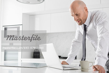 Mid adult businessman using laptop at kitchen counter