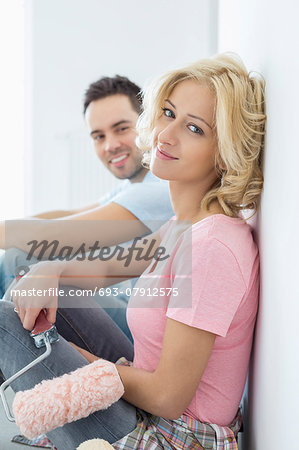 Portrait of beautiful woman holding paint roller with man in background