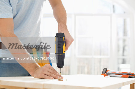 Midsection of man drilling nail on table