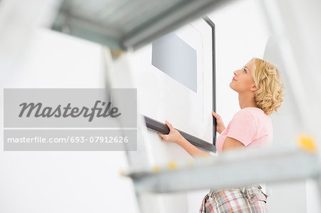 Woman positioning picture frame on wall Woman positioning picture frame on wall