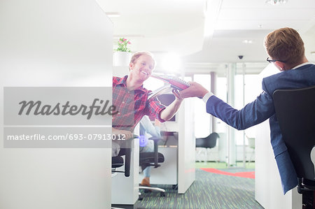 Rear view of businessman giving files to colleague in creative office