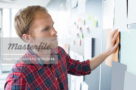 Young businessman reading documents on wall at creative office