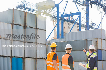 Rear view of workers inspecting cargo containers in shipping yard