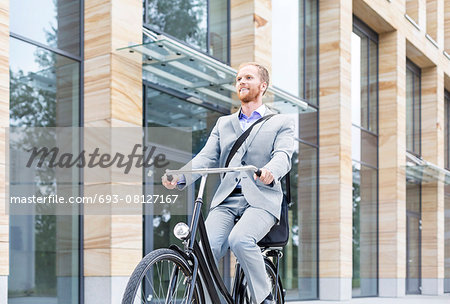 Smiling businessman riding bicycle outside building