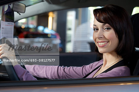 Portrait of young woman sitting in driver's seat at car dealersh