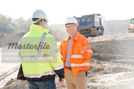 Happy engineer talking to colleague at construction site on sunny day