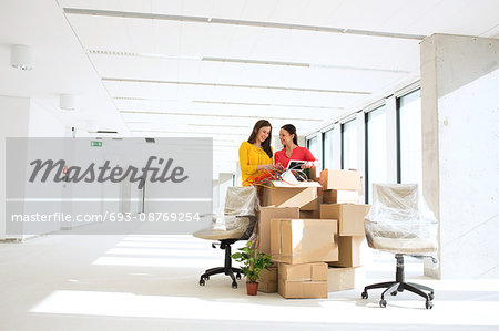 Businesswomen unpacking cardboard boxes in new office