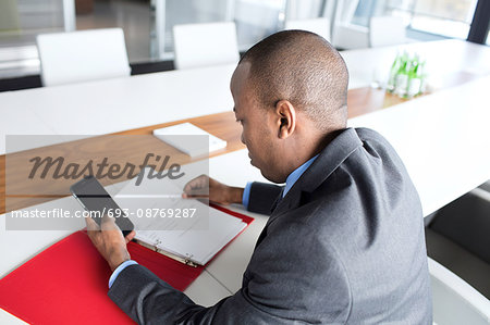 High angle view of young businessman with file using mobile phone at conference table