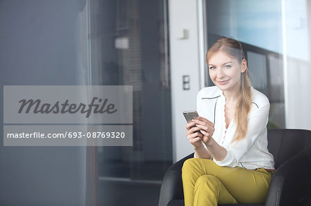 Portrait of confident young businesswoman using mobile phone on chair in office