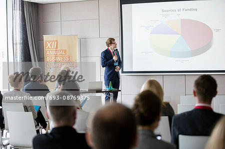 Businessman explaining pie chart to audience in seminar hall