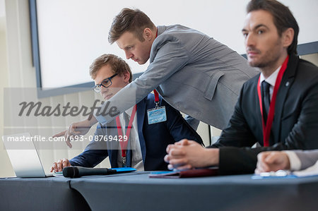 Businessman explaining strategy to colleague on laptop in convention center