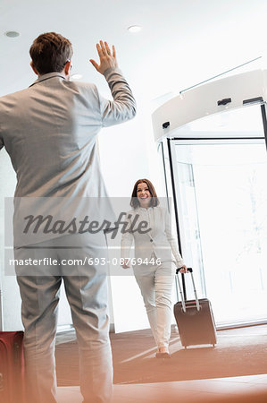 Cheerful businesswoman with luggage walking towards male colleague in convention center