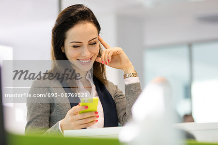 Smiling young businesswoman reading text message on smartphone at office