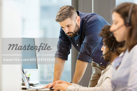 Mid adult businessman using laptop with colleagues wearing headsets in office