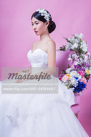 Elegant bride looking away while sitting on chair against pink background