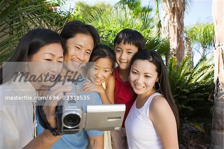 Family Looking at Video Camera Screen in back yard, front view