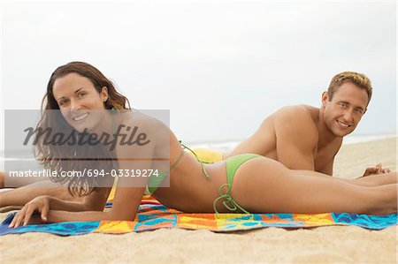 Young couple lying down on beach on towel, portrait, side view