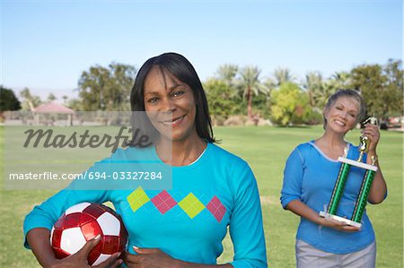 Senior women holding soccer ball and trophy in park, portrait