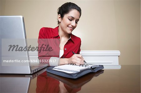 Business woman writing in diary beside laptop in office