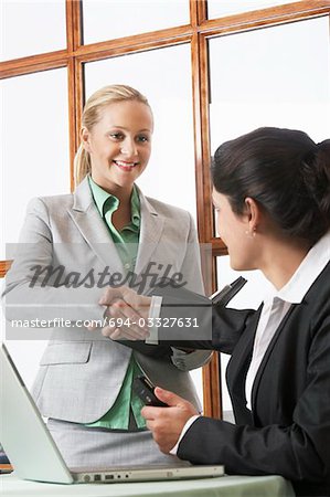 Two business women shaking hands in office