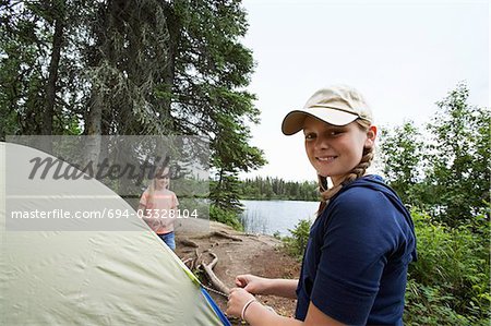 Two teenage girls standing by tent near lake, portrait
